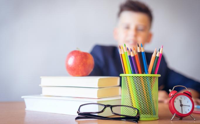 Child sitting behind books, apple and colored pencils 